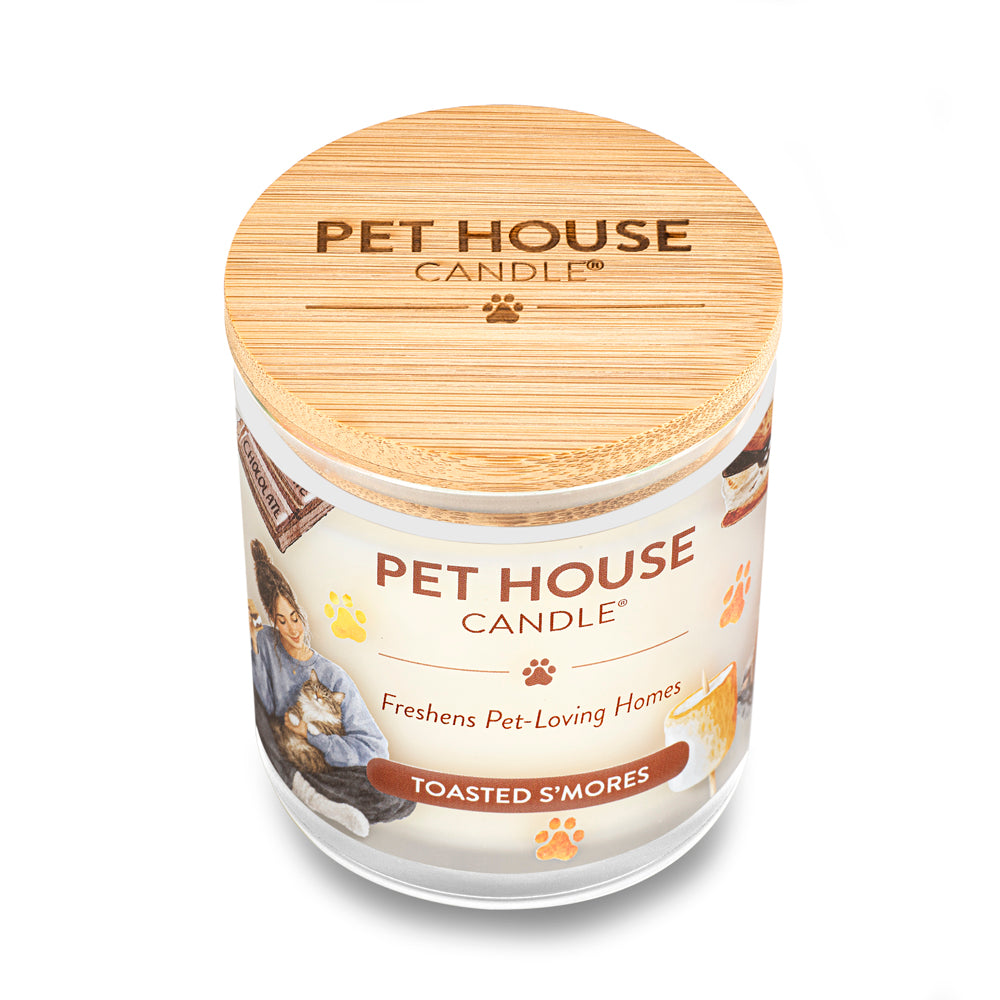 A Pet House Candle in a clear glass jar with a light natural wood lid and a cream-colored label featuring a cat illustration and the scent name 'Toasted S'mores'.